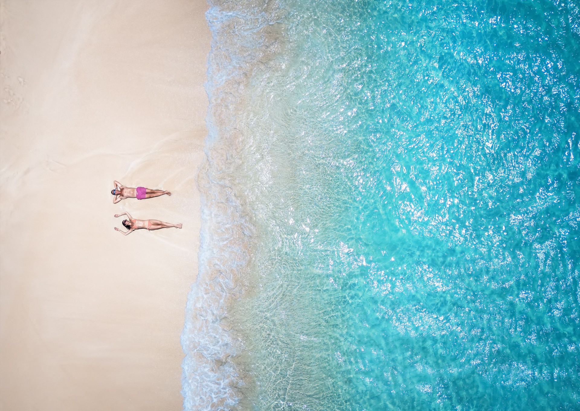 Aerial top down view of a couple in swimsuits sunbathing on a beautiful tropical beach